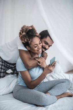 Adam yatakta selfie çeken kadına sarılıyor.