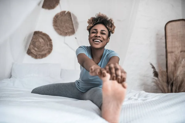 Ridendo donna seduta sul letto chinandosi alla gamba — Foto Stock