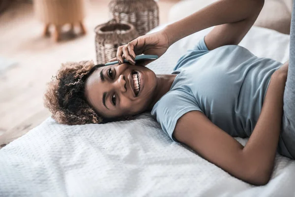Веселая африканская американка со смартфоном на кровати — стоковое фото
