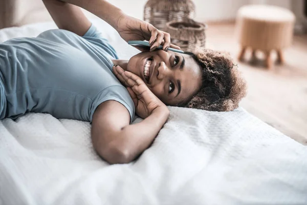 Glädjande kvinna talar på smartphone liggande på sängen — Stockfoto