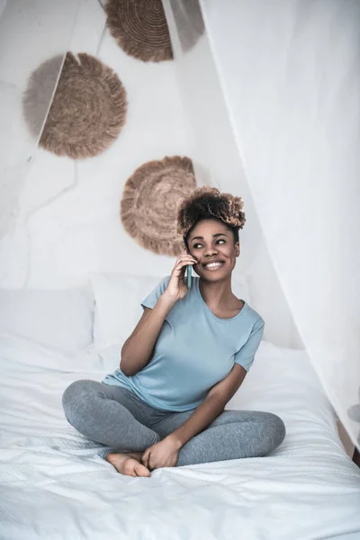 Šťastná žena mluví na smartphone sedí na posteli — Stock fotografie