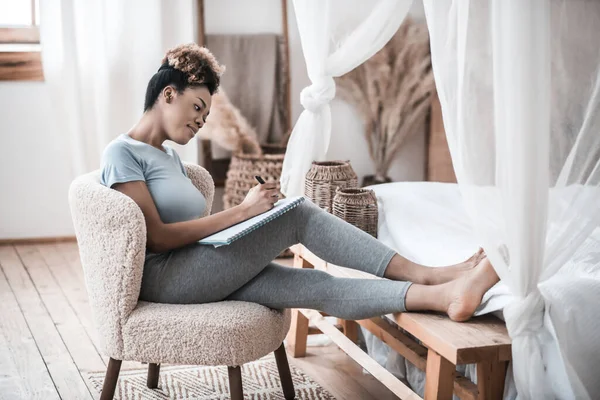 Woman sitting in chair at home writing notes