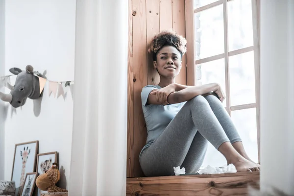 Deprimerad ung mörkhyad kvinna som sitter på fönsterbrädan — Stockfoto