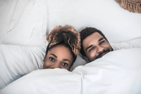 Улыбающиеся мужчина и женщина лежат под одеялом — стоковое фото