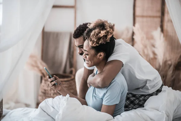 Africano americano abraço esposa olhando para o smartphone — Fotografia de Stock