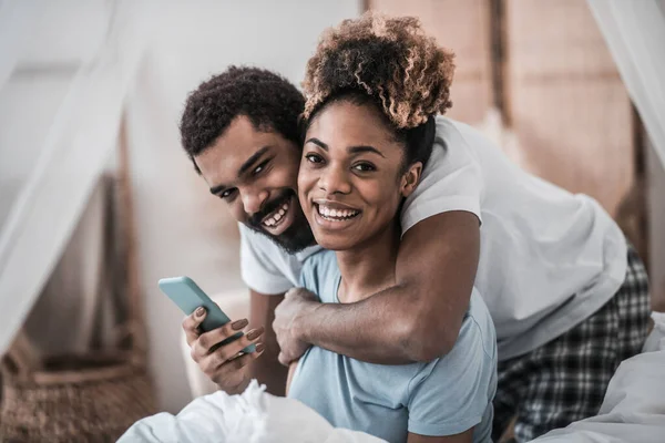 Ung mörkhyad man och hustru i pyjamas med smartphone — Stockfoto