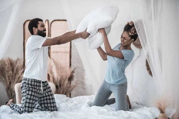 Manžel a manželka bojují polštáře na posteli — Stock fotografie