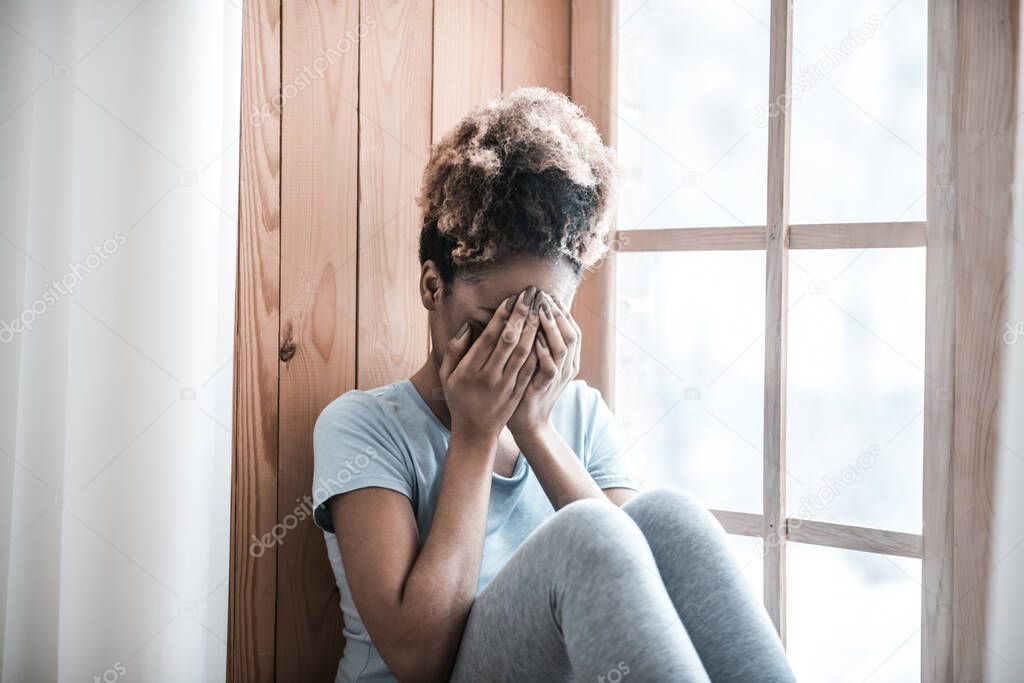 Upset dark skinned woman covering face with hands