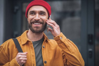 Kırmızı şapkalı ve turuncu ceketli adam mutlu görünüyor.