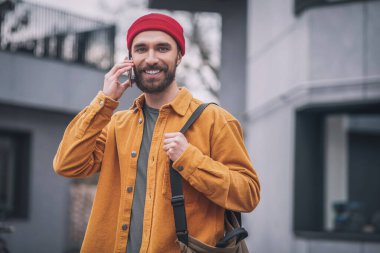 Kırmızı şapkalı ve turuncu ceketli adam mutlu görünüyor.