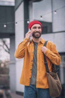 Kırmızı şapkalı ve elinde akıllı telefonuyla turuncu ceketli bir adam.
