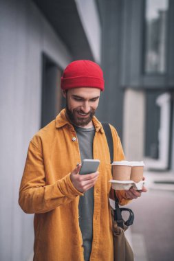Elinde kahve fincanları tutan kırmızı şapkalı genç sakallı adam.