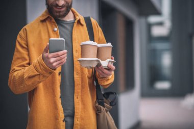 Elinde kahve fincanları tutan kırmızı şapkalı genç sakallı adam.