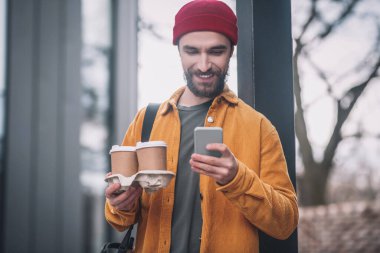 Elinde kahve fincanları tutan kırmızı şapkalı genç sakallı adam.