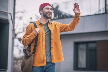 Turuncu ceketli genç adam biriyle tanışıyor ve elini sallıyor.