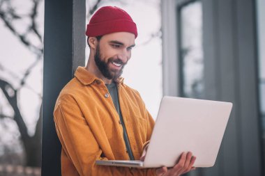 Kırmızı şapkalı, laptoplu sakallı genç adam.