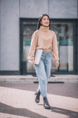 Genç Asyalı kadın dizüstü bilgisayar tutuyor ve kendinden emin görünüyor.