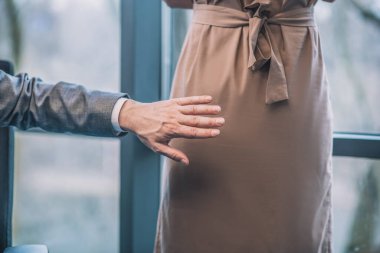 Erkek eli kameraya çevrilmiş bir kadının yanında duruyor.