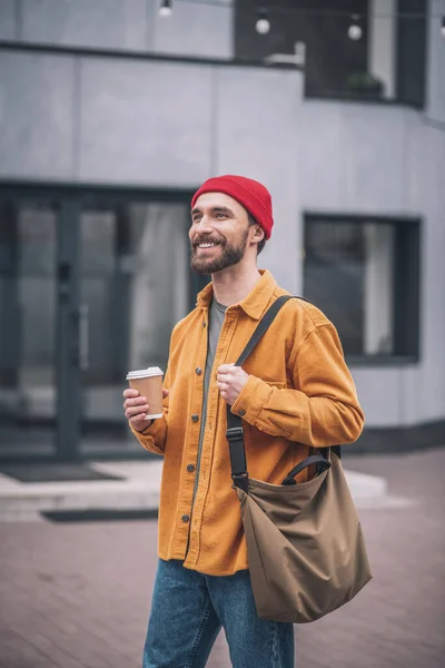 Pria bertopi merah dan jaket oranye dengan cangkir kopi di tangan — Stok Foto