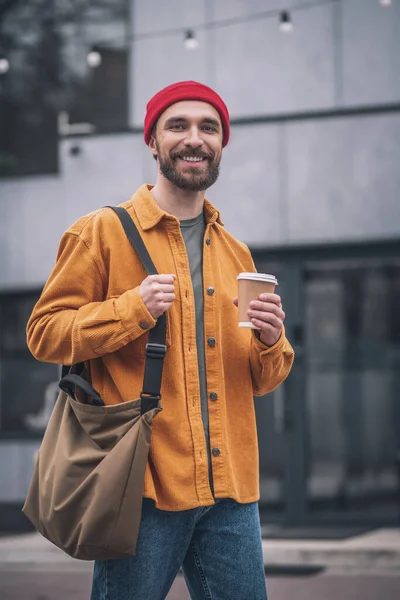 Man i röd hatt och orange jacka med kaffekopp i händerna — Stockfoto