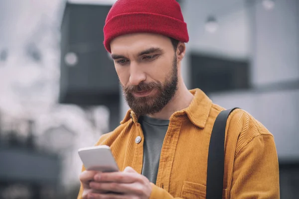 Hombre con un sombrero rojo sosteniendo su teléfono y enviando un mensaje —  Fotos de Stock