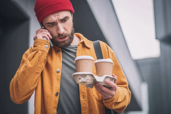 Joven barbudo con sombrero rojo sosteniendo tazas de café —  Fotos de Stock