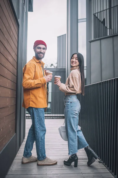 Jovem e mulher em roupas casuais que parecem positivas enquanto toma café fora — Fotografia de Stock