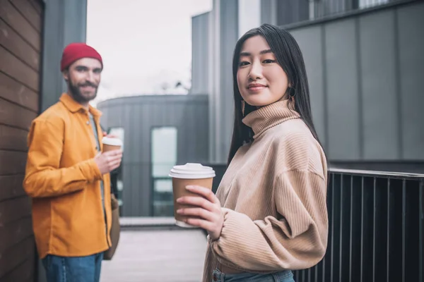 Jovem e mulher em roupas casuais que parecem positivas enquanto toma café fora — Fotografia de Stock