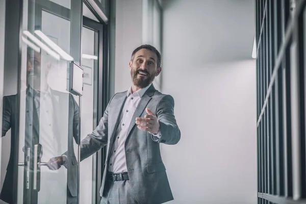 Hombre alegre en traje gesto saludo cerca de la puerta de la oficina — Foto de Stock