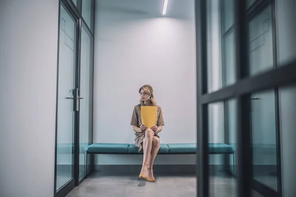 Mujer en vestido con carpeta sentada en pasillo de oficina —  Fotos de Stock