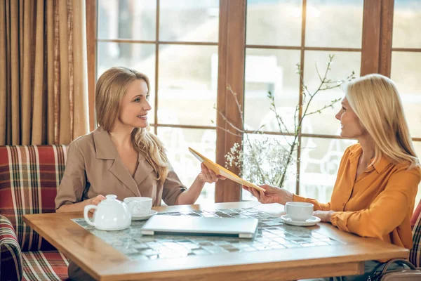 Två kvinnor pratar och diskuterar något när de sitter vid bordet på ett kafé — Stockfoto