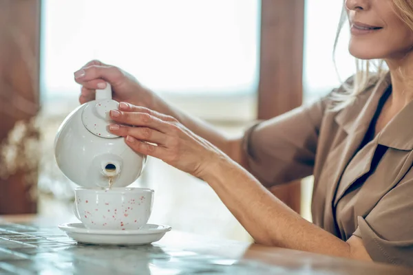 A pretty woman pouring tea from the tea pot to the cup — Stock Photo, Image