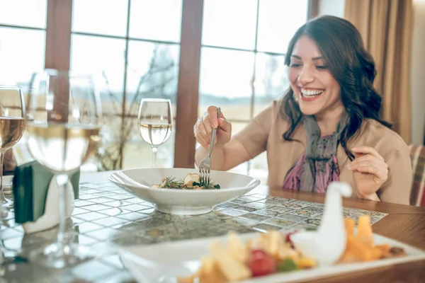 Femme mignonne aux cheveux bruns assis à la table dans un restaurant et regardant heureux — Photo