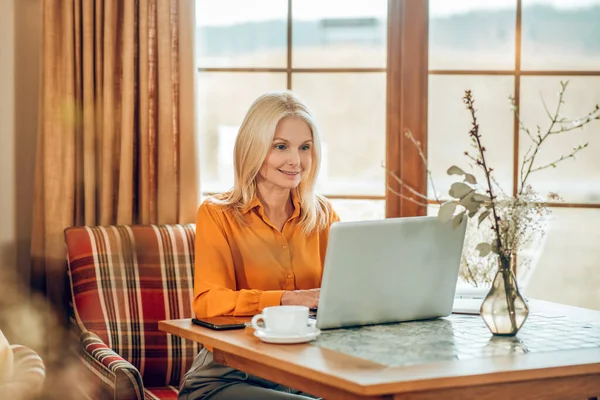 Blondýny dlouhosrstá žena sedí u stolu a pracuje na notebooku — Stock fotografie