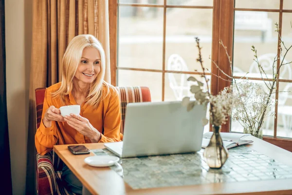 Blondýny dlouhosrstá žena sedí u stolu a pracuje na notebooku — Stock fotografie