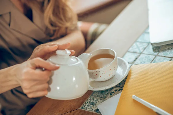 Woman pouring tea to the cup from a white tea pot — Stock Photo, Image