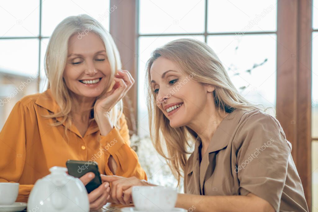 Two cute ladies spending time together and discussing photos in a smartphone