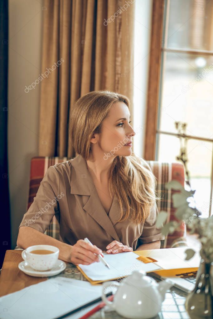 Blonde long-haired woman sitting at the table and looking thoughtful