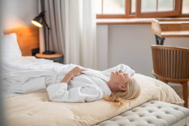 Beyaz banyolu güzel bir kadın yatağa uzanıyor.