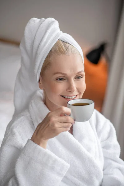 Piękna kobieta w białym szlafroku pijąca kawę po kąpieli — Zdjęcie stockowe