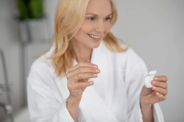 Una mujer guapa y sonriente limpiándose los dientes con un hilo dental — Foto de Stock