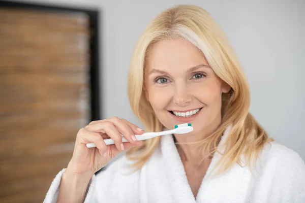 Mujer rubia sonriente cepillándose los dientes y luciendo feliz — Foto de Stock