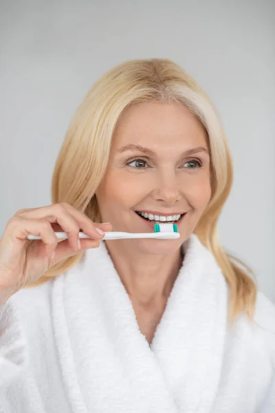 Leende blond kvinna borsta tänderna och ser glad ut — Stockfoto