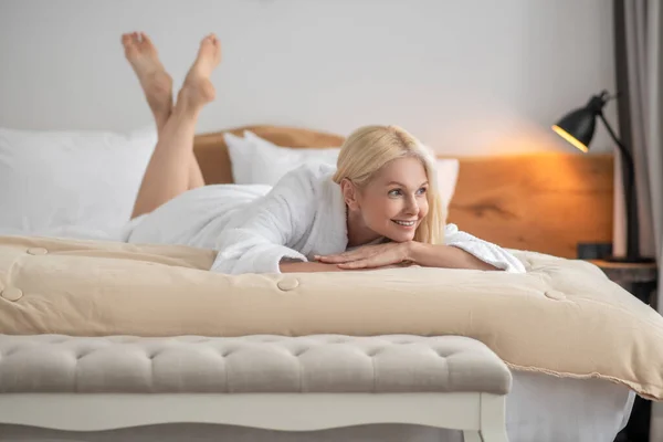 Una hermosa mujer en una bata blanca acostada en una cama — Foto de Stock