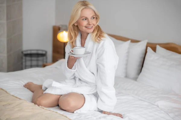 Mooie blonde vrouw met haar ochtendthee in de slaapkamer — Stockfoto