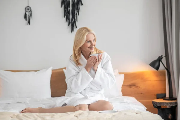Pretty blonde woman having her morning tea in the bedroom