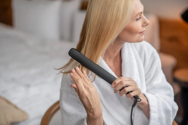 Mujer bonita rubia haciendo peinado mediante el uso de una plancha plana — Foto de Stock