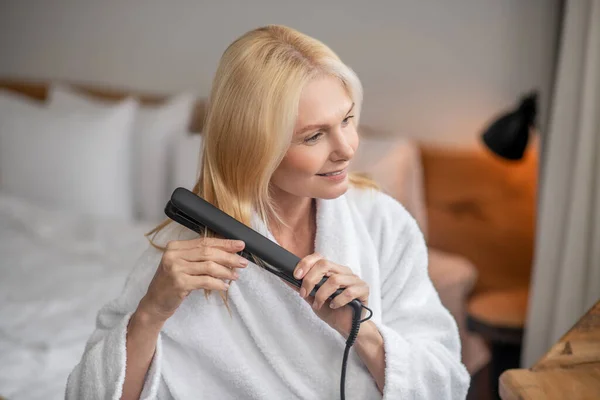 Blonde pretty woman making hairstyling by using a flat iron — Stock Photo, Image