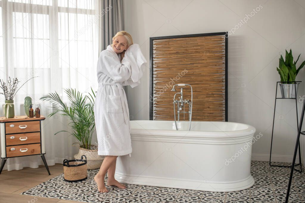 Smiling blonde woman drying her hair with a towel after the bath