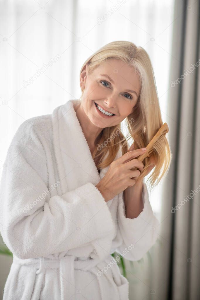 Adorable woman brushing her hair and looking relaxed